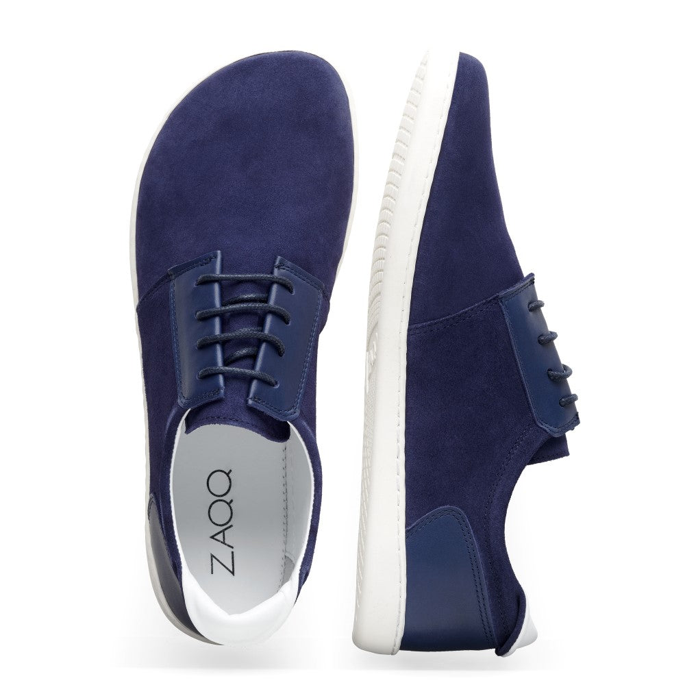 Ein Paar PIQUANT dunkelblaue Sneaker mit weißer Sohle, von oben und von der Seite betrachtet. Der linke Schuh trägt auf der Innenseite den Markennamen ZAQQ. Dieses Veloursleder-Design ist elegant und lässig, mit Schnürverschlüssen und einer minimalistischen Ästhetik, die perfekt zu einem entspannten Stil passt.