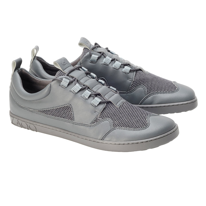 Ein Paar stylische ZAQQ QARLY Grey Sneaker aus Mesh und veganem Leder mit markanten Schnürsenkelschlaufen und geschmeidiger Sohle. Die Sneaker sind kunstvoll schräg vor einem weißen Hintergrund platziert.