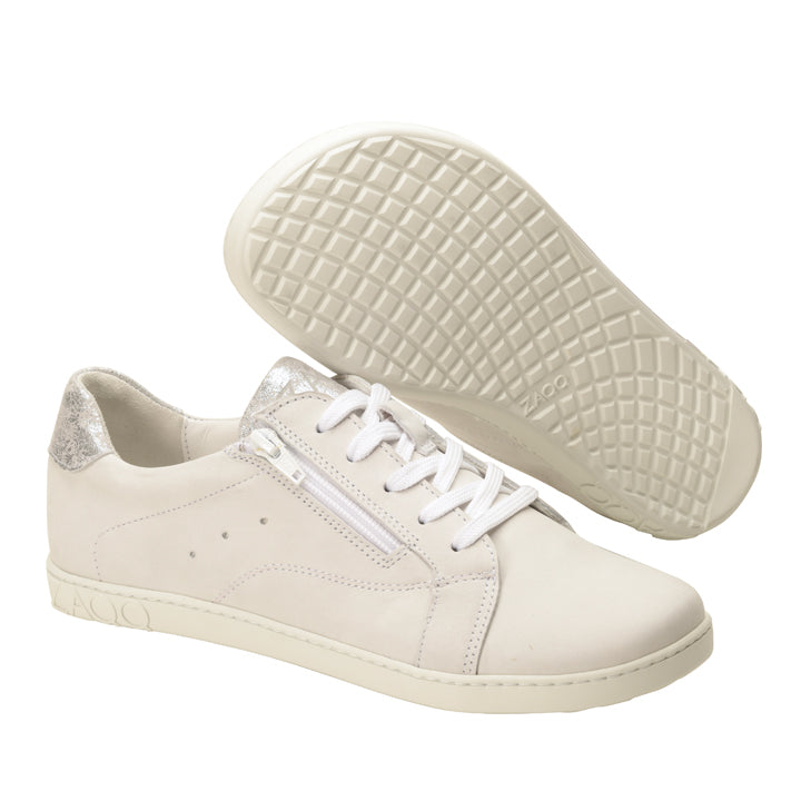 Wir präsentieren die QOMFY Wide White Sneakers von ZAQQ – ein schickes Paar aus Nappaleder mit silbernen Akzenten an der Ferse. Diese stylischen Schuhe haben weiße Schnürsenkel, einen praktischen seitlichen Reißverschluss und ein strukturiertes Sohlenmuster. Ein Schuh steht aufrecht, während der andere auf seiner Sohle positioniert ist, um das aufwendige Profildesign zu präsentieren.