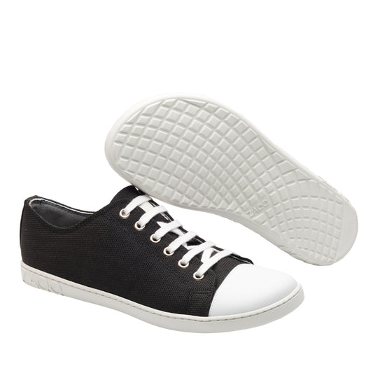 Die ZAQQ CHUQQS Low Black Sneaker bestechen durch ihr stylisches schwarzes Canvas-Design mit kontrastierenden weißen Gummisohlen und Schnürsenkeln. Ein Schuh wird aufrecht präsentiert, um das strukturierte Sohlenmuster hervorzuheben, während das schwarze Denim-Design des anderen Schuhs für zusätzliches Flair sorgt.