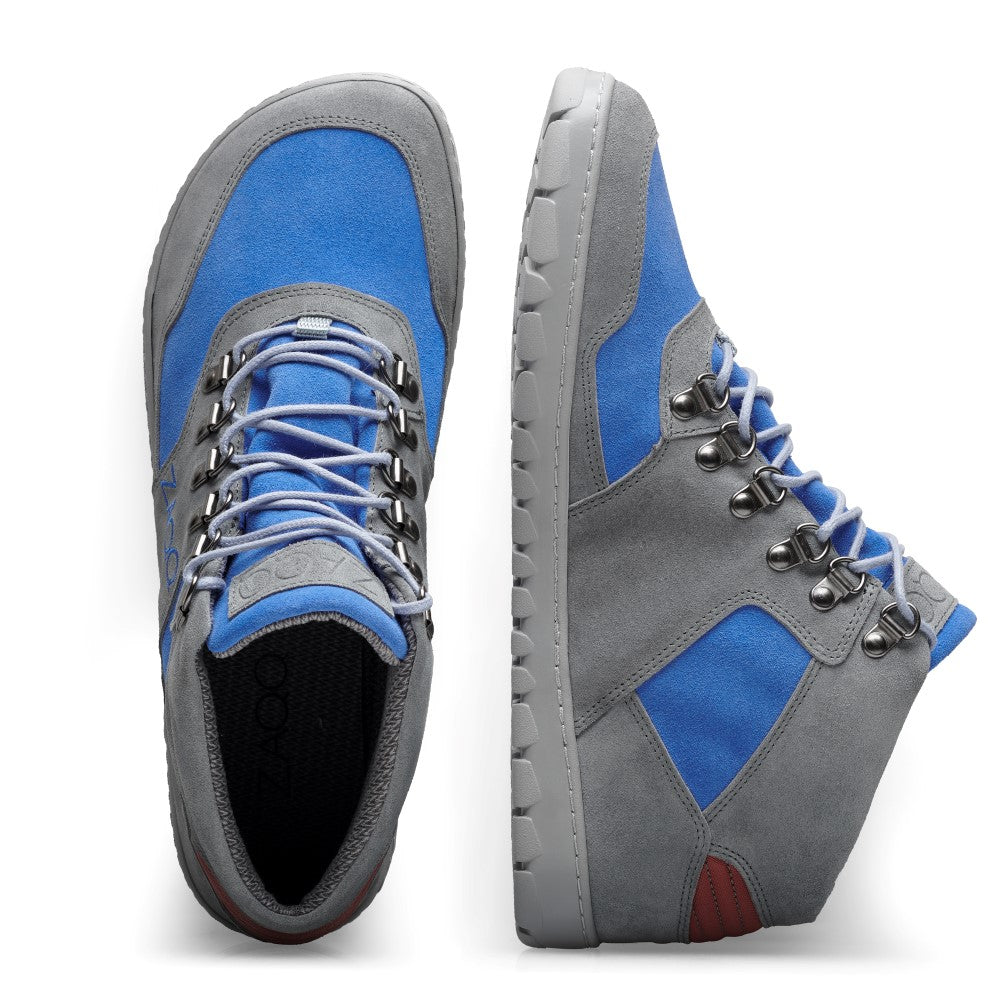 Wir präsentieren den HIQE Mid Azure Waterproof von ZAQQ: Diese stylischen High-Top-Sneaker sind fachmännisch aus Veloursleder in einer auffälligen Kombination aus Blau und Grau gefertigt. Die Schuhe verfügen über Metallösen, graue Schnürsenkel und eine robuste Outdoorsohle für Stil und Funktionalität. Der Markenname ist elegant auf der Zunge des Schuhs eingeprägt.