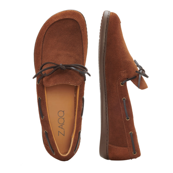 Wir präsentieren den QEA Velours Cognac, ein Paar braune Wildleder-Loafer mit Schnürsenkeln von ZAQQ. Diese Schuhe, elegant in Draufsicht und Seitenansicht präsentiert, verfügen über ein hellbraunes Innenfutter, auf dem der Markenname ZAQQ dezent für zusätzliche Eleganz angebracht ist. Die dunkelbraunen Sohlen heben den raffinierten Stil dieser eleganteren Herrenschuhe noch weiter hervor.