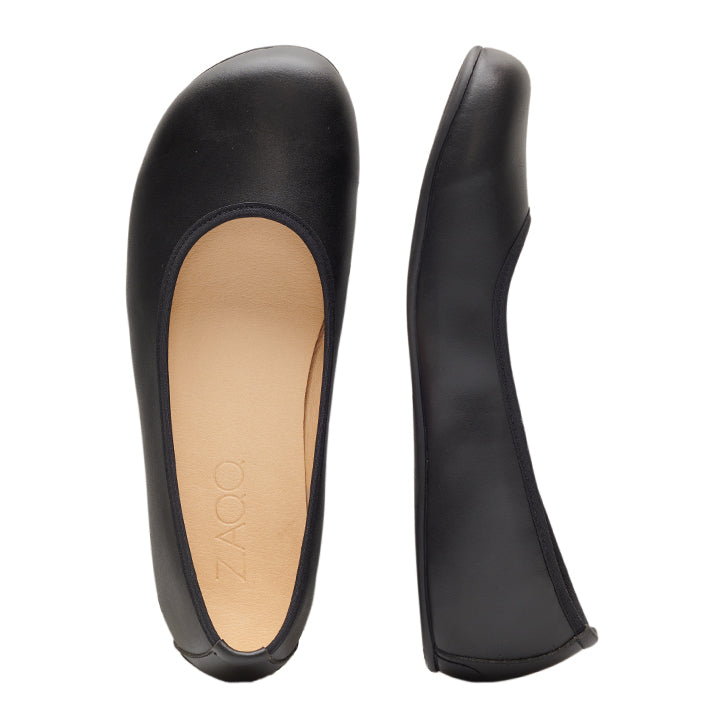 Ein Paar QARMA Vegan Black Ballerinas von ZAQQ mit abgerundeter Zehenpartie aus veganem Leder. Ein Schuh ist von oben zu sehen und zeigt die Innensohle mit dem Markennamen ZAQQ, während der andere von der Seite zu sehen ist, um sein elegantes Profil und sein atmungsaktives Material hervorzuheben.