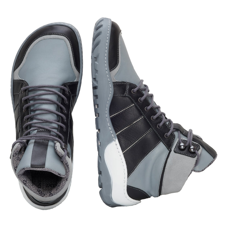 Wir präsentieren die ZAQQ MONTBLANQ Grey Waterproof Sneaker: ein stilvolles Paar High-Top-Schuhe in Grau und Schwarz mit weißen Akzenten, gefertigt für einen sportlichen Look. Der linke Schuh ist von oben zu sehen, während der rechte Schuh angewinkelt ist, um seine rutschfeste Sohle und das elegante Barfußschuh-Design hervorzuheben. Ideal für jedes Abenteuer.