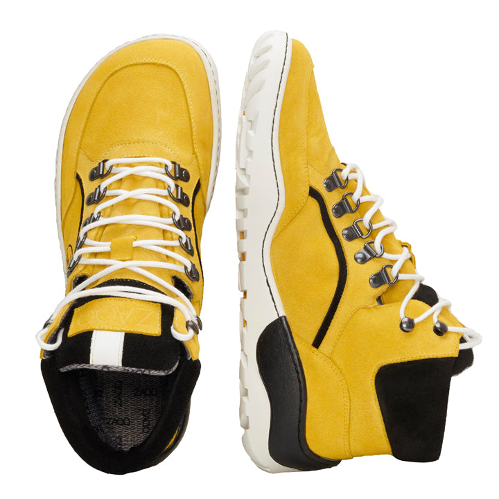 Ein Paar ZAQQ TREQ Yellow Waterproof Wildleder-Sneaker mit schwarzen Akzenten und weißen Schnürsenkeln. Diese Barfußschuhe haben eine klobige TERRA-Sohle und Metallösen und bieten ein robustes und stilvolles Erscheinungsbild. Ein Schuh ist von der Seite abgebildet, während der andere von oben gezeigt wird.