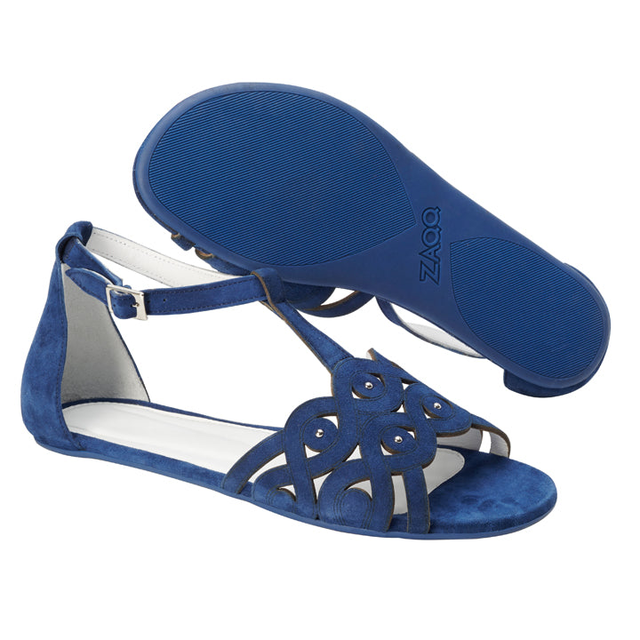 Die BOUQET Blue Sandalen von ZAQQ bestehen aus blauem Wildleder mit aufwendigen, ausgeschnittenen Wirbelmustern. Eine Sandale steht aufrecht und betont die offene Spitze und den Knöchelriemen für außergewöhnlichen Tragekomfort, während die andere umgedreht ist und die strukturierte Sohle mit dem stolzen ZAQQ-Logo zeigt – erleben Sie ihre Eleganz aus erster Hand.