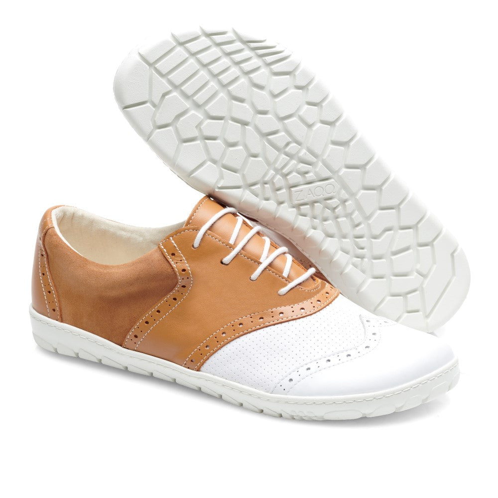 Wir präsentieren den LINQ Golf Brown Waterproof von ZAQQ: Ein Paar Oxford-Schuhe aus Leder im klassischen Golfschuh-Design, das ein stilvolles Farbschema in Weiß und Braun aufweist. Diese Schuhe verfügen über dekorative Perforationen und sind mit weißen Schnürsenkeln ausgestattet. Ein Schuh steht aufrecht, während der andere mit der Sohle nach oben positioniert ist, wodurch seine strukturierte weiße Sohle hervorgehoben wird.