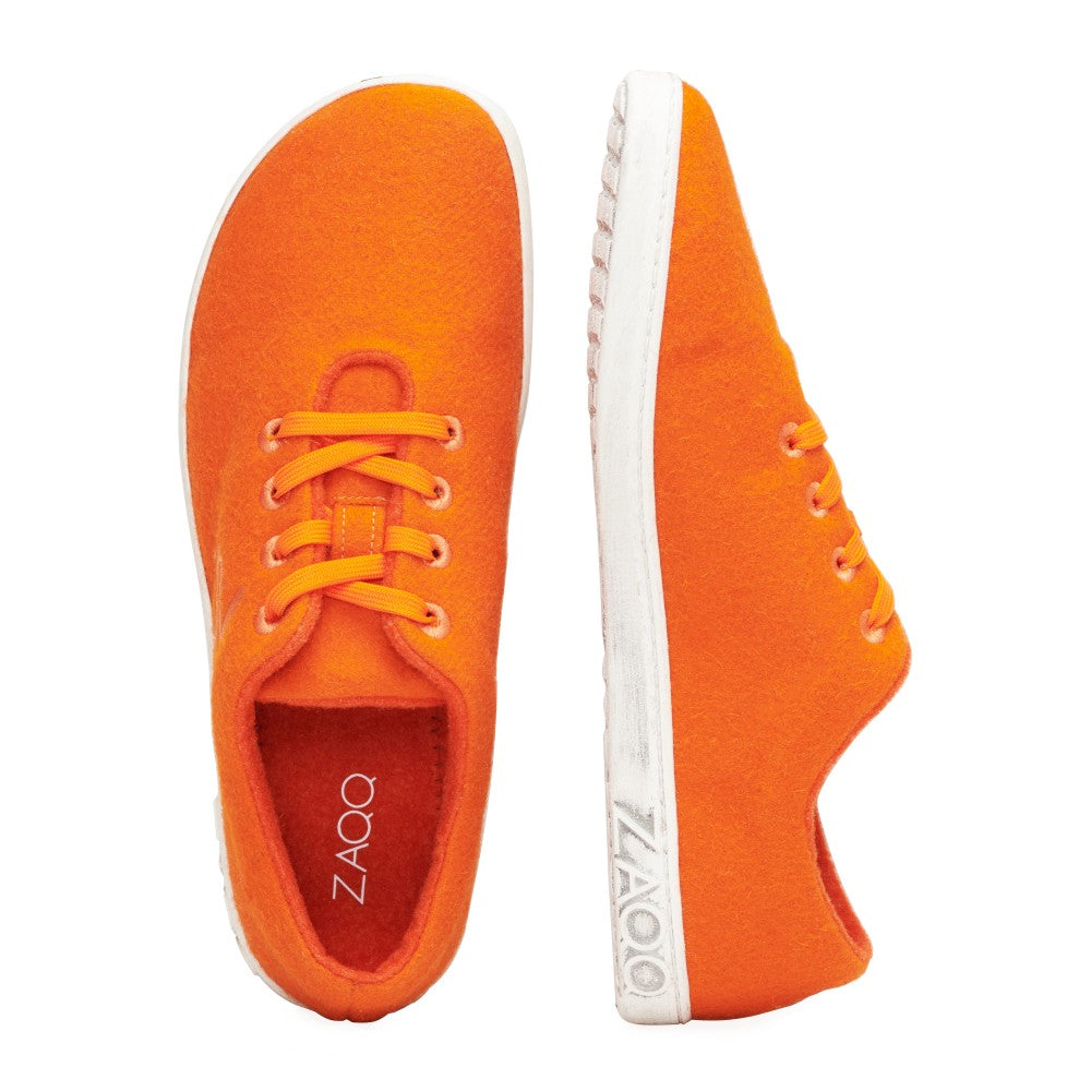 Die LIQE Orange Sneaker von ZAQQ zeichnen sich durch eine auffällige leuchtend orange Farbe mit weißen Sohlen aus. Ein Sneaker ist von oben und der andere von der Seite zu sehen, wobei die leuchtend orangefarbenen Schnürsenkel und das ZAQQ-Logo an der Seite hervorgehoben werden. Diese Sneaker wurden für ein Barfußgefühl konzipiert und bieten außergewöhnlichen Komfort und Freiheit bei jedem Schritt.