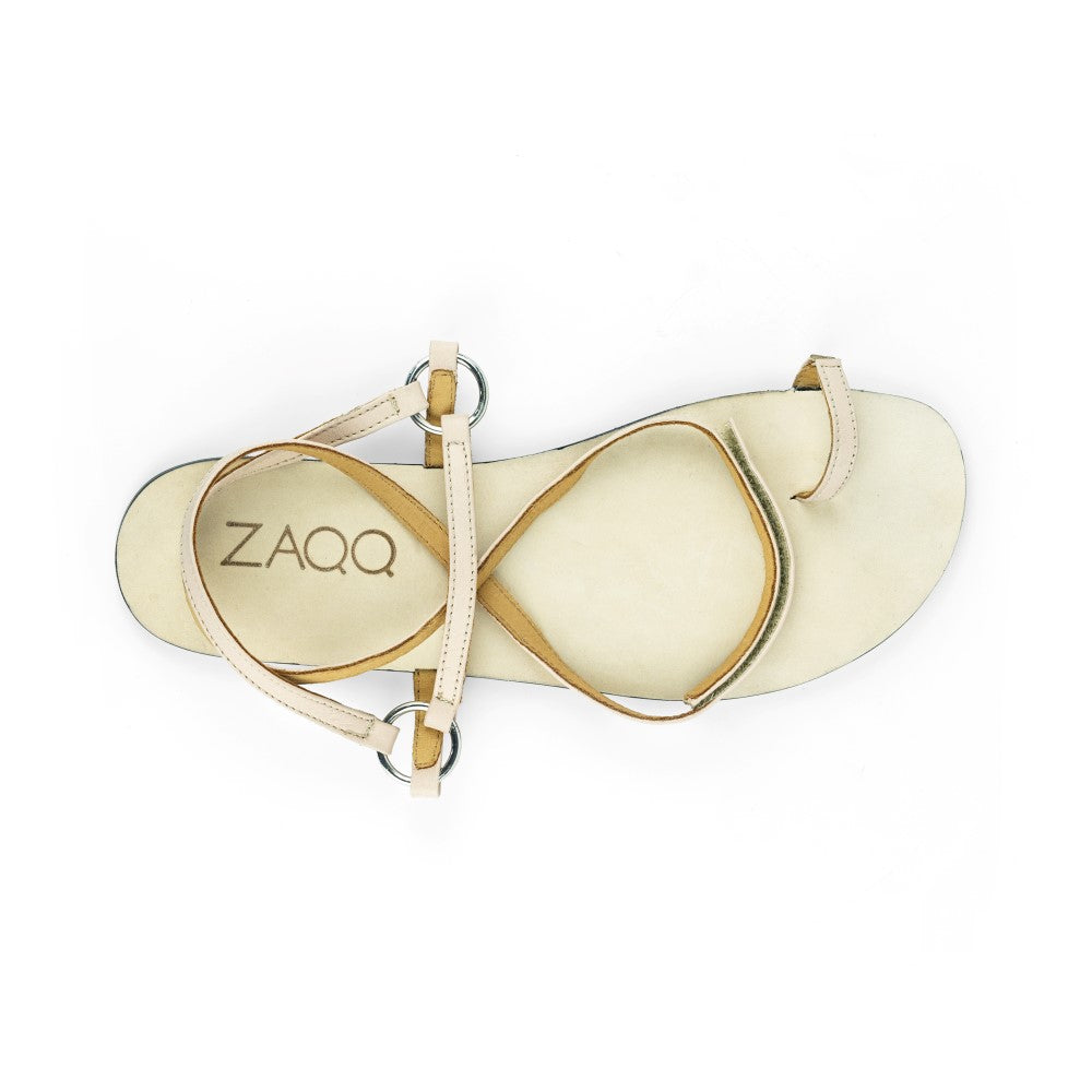 Die MINIQ Nude Barfuß-Sandale von ZAQQ besticht durch eine beige Farbe mit minimalistischen Riemen und kreisförmigen Metallakzenten aus hochwertigem Nappaleder. Das ZAQQ-Logo ist auf der Innensohle dezent vor einem strahlend weißen Hintergrund abgesetzt.