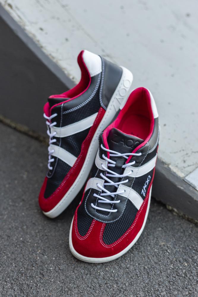 Die modischen ZAQQ OAQLEY Red Sneaker bestechen durch ihr auffälliges rot-schwarz-weißes Design. Diese Sportschuhe sind mit weißen Schnürsenkeln ausgestattet und zeigen das Branding an der Seite. Sie sind anmutig auf einem strukturierten Bürgersteig neben einer Betonkante positioniert.