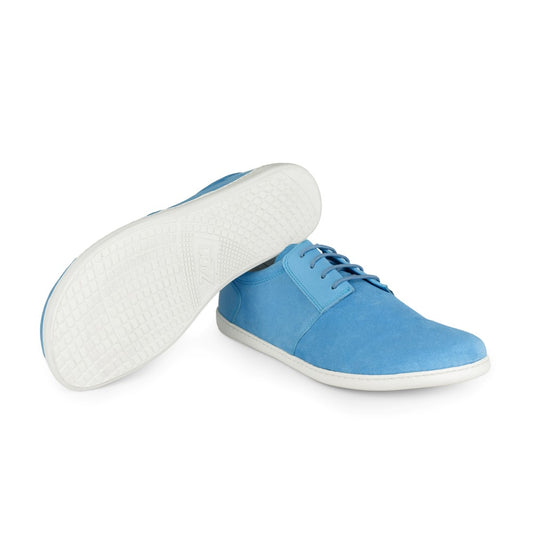 Ein Paar PIQUANT Azure-Sneaker von ZAQQ in blauem Design mit weißer Sohle. Ein Schuh steht aufrecht und zeigt seine Schnürsenkel und aufwendigen Nähte, während der andere geneigt ist und eine strukturierte Sohle mit einem Gittermuster zeigt.