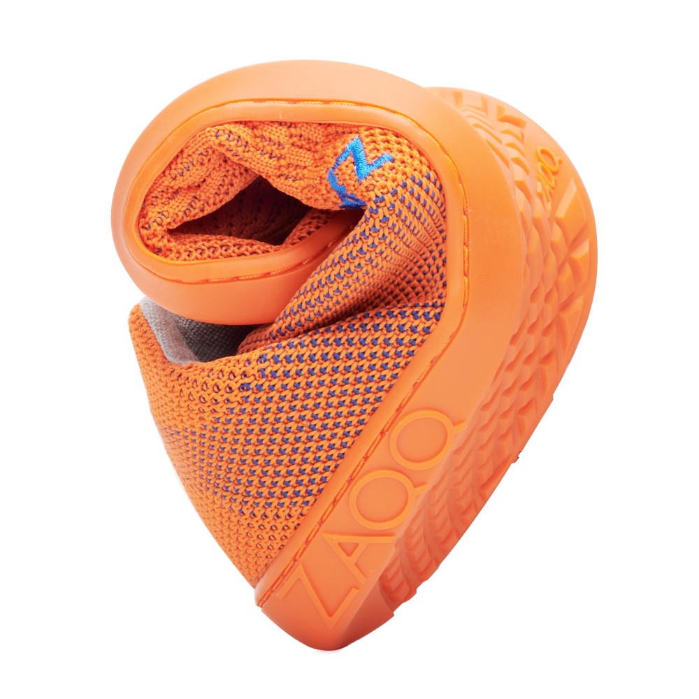 Der QNIT Orange von ZAQQ ist ein leichter Sportschuh, der in einer kompakten Spiralform präsentiert wird, was seine Flexibilität unterstreicht. Er besteht aus atmungsaktivem veganem Strickgewebe und einer strukturierten Gummisohle, wobei das ZAQQ-Branding an der Seite deutlich zu sehen ist.