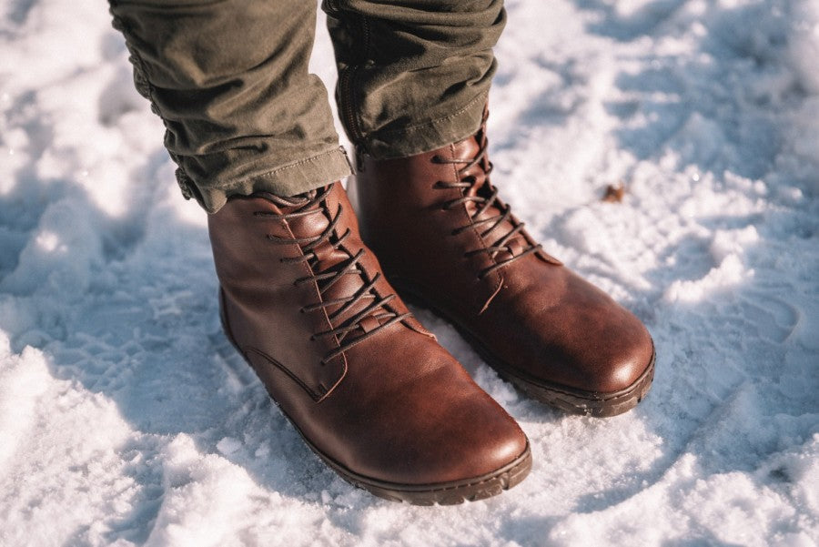 Eine Nahaufnahme zeigt eine Person, die QUINTIC Winter Vegan Nut-Lederstiefel von ZAQQ mit olivgrünen Hosen trägt und auf verschneitem Gelände steht. Der vegane Schnürschuh verfügt über eine robuste Sohle, die für optimale Leistung unter winterlichen Bedingungen ausgelegt ist.