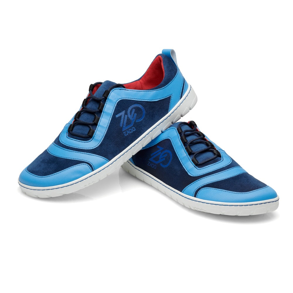 Wir präsentieren die SQILL Ocean Sneaker von ZAQQ in Blau und Marine mit weißer Sohle und rotem Innenfutter. Sie sind in einem superleichten Stil gestaltet und zeigen stolz ein Logo an der Seite. Die Sneaker sind kreativ positioniert, indem ein Schuh an den anderen gelehnt wird.