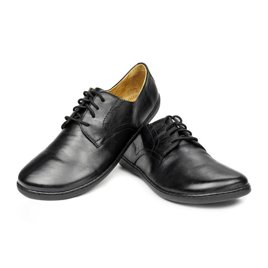 Ein Paar PEAQ Black-Schuhe von ZAQQ, elegant präsentiert vor einem weißen Hintergrund. Diese sorgfältig gefertigten Schuhe zeichnen sich durch eine polierte Oberfläche und ein klassisches Design aus, wobei ein Schuh sanft auf dem anderen lehnt, um ihre bequeme Passform und zeitlose Attraktivität hervorzuheben.