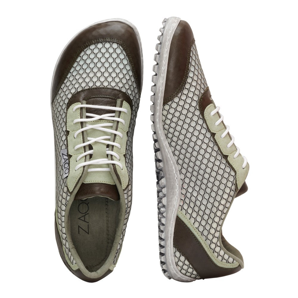 Wir präsentieren den TOQIO Light Green von ZAQQ – ein stylisches Paar Barfuß-Sneaker aus weißem und grünem Mesh-Gewebe mit geometrischem Muster. Diese Sneaker zeichnen sich durch elegante Akzente aus braunem Nappaleder und strahlend weiße Schnürsenkel aus. Die Sohle ist mit einem strukturierten Griff für bessere Traktion ausgestattet. Auf dem Bild steht ein Schuh aufrecht, während der andere auf der Seite liegt, was ihre außergewöhnliche Atmungsaktivität zur Schau stellt.