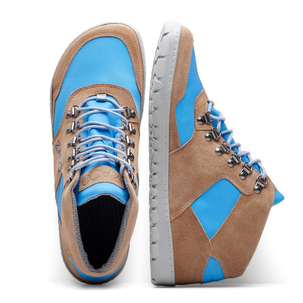 Wir präsentieren den HIQE Mid Sky Waterproof von ZAQQ: Diese stylischen Sneaker mit Einsätzen aus blauem und braunem Wildleder sind als vielseitige Wanderschuhe konzipiert. Ein Schuh liegt flach, der andere steht auf der Seite. Sie sind mit Metallösen und dicken Schnürsenkeln versehen und ruhen elegant auf einem weißen Hintergrund.