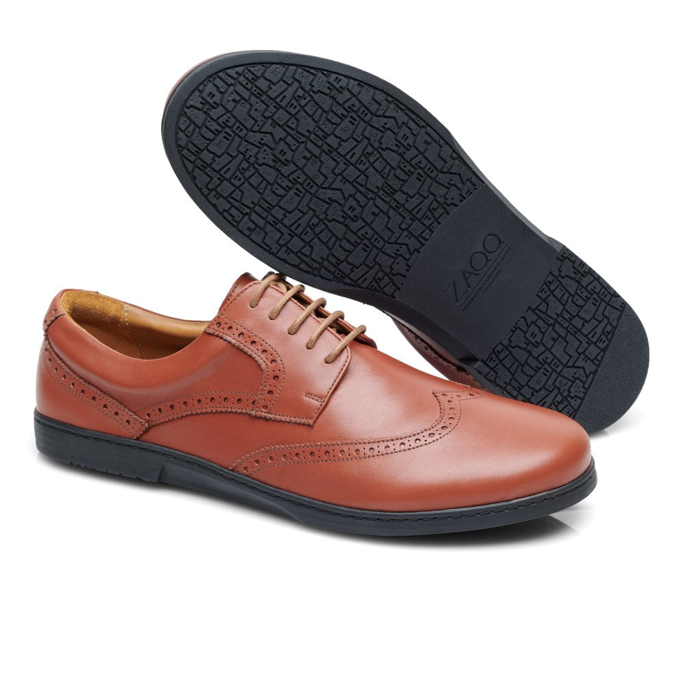 Der BRIQ Brogue Cognac von ZAQQ ist ein Paar stilvoller Business-Schuhe aus braunem Leder mit schwarzen Gummisohlen. Ein Schuh steht aufrecht und zeigt seine elegante Seite und sein klassisches Obermaterialdesign, während der andere auf der Seite liegt und die strukturierte Sohle freigibt.